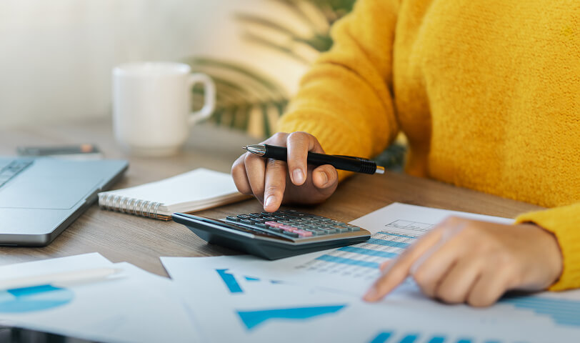 Real estate agent working at a desk covered with spreadsheets, using a calculator.