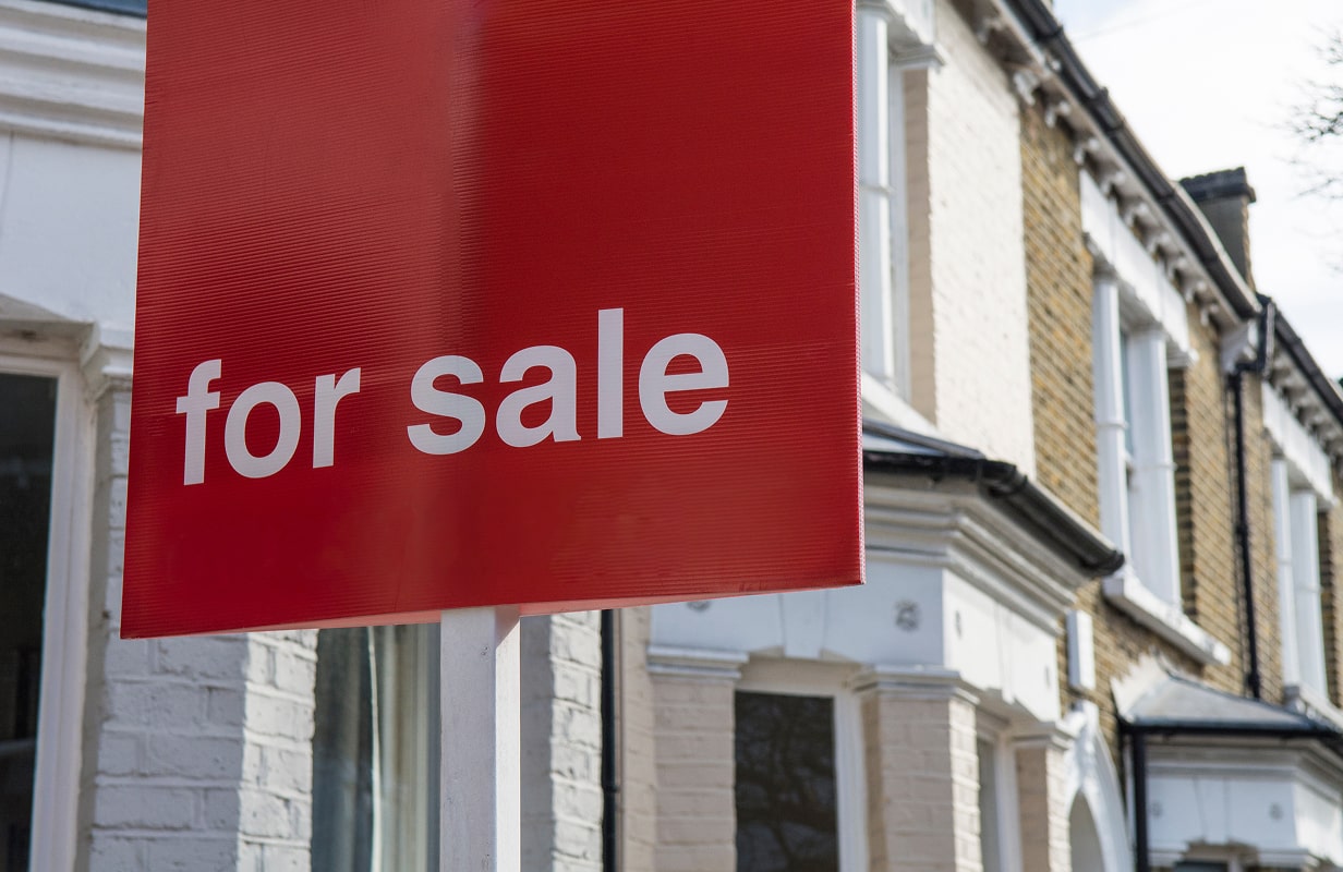 Close-up of a red 'For Sale' sign outside a property.